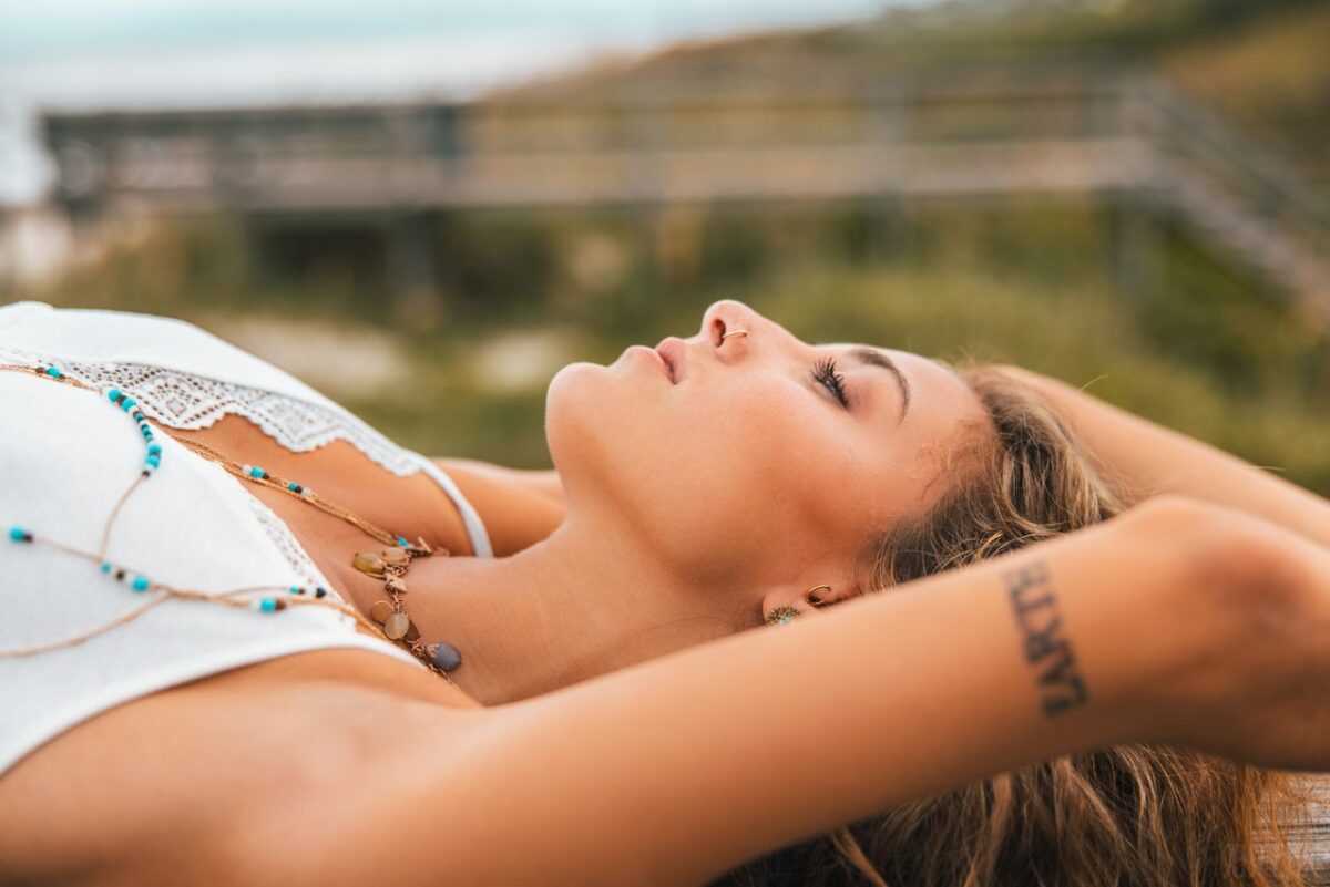 portfolio-04 Young woman with tattoo lying outdoors, arms raised, in a peaceful pose.
