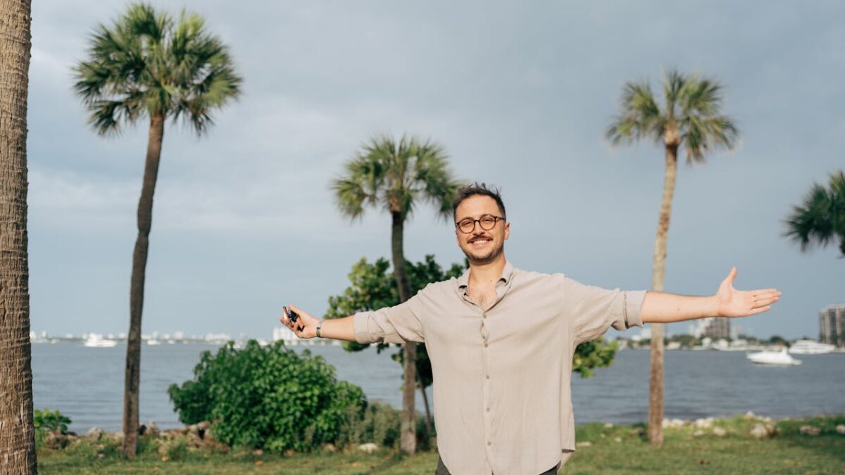 core-values Smiling man with open arms outdoors by palm trees and water.