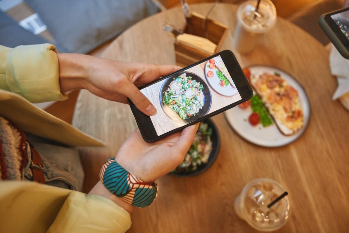 portfolio-05 Person taking a photo of delicious meals on a smartphone in a cozy cafe setting.